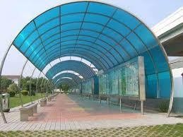 Long arched outdoor walkway canopy featuring blue translucent polycarbonate roofing panels supported by a curved metal frame.