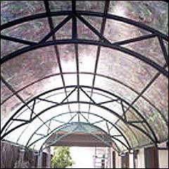 Arched outdoor metal canopy frame fitted with floral-patterned PP translucent roofing sheets over a walkway.