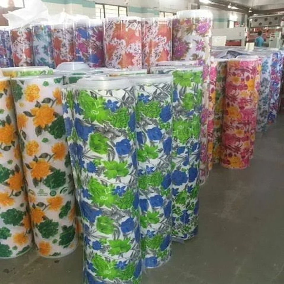Multiple rolls of floral-printed polypropylene roofing and main gate sheets standing upright in a factory warehouse.