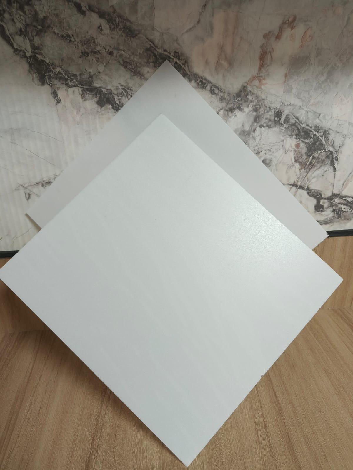 Two square white LED diffuser sheets arranged diagonally against a marble and wooden backdrop.